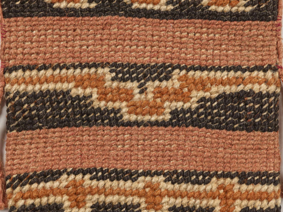 Detail of the patterning on a black and terracotta striped woven bag. On the black stripes, orange geometric patterns are framed by cream threads.