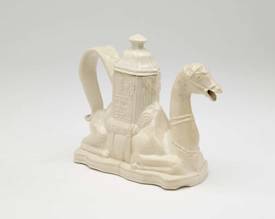 A cream colored teapot in the shape of a camel with a hexagonal lid.