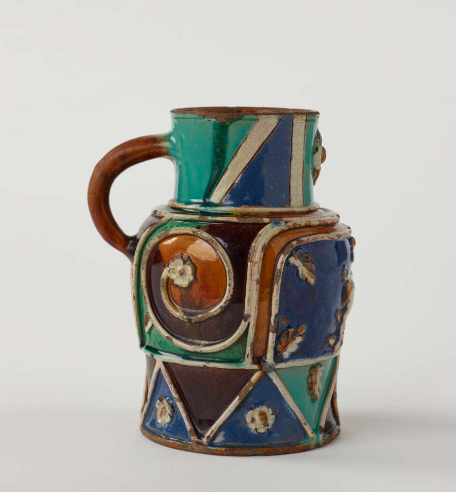 A lead-glazed pitcher with white, blue, turquoise, orange, and black decorations. Some of the white decorations are raised.