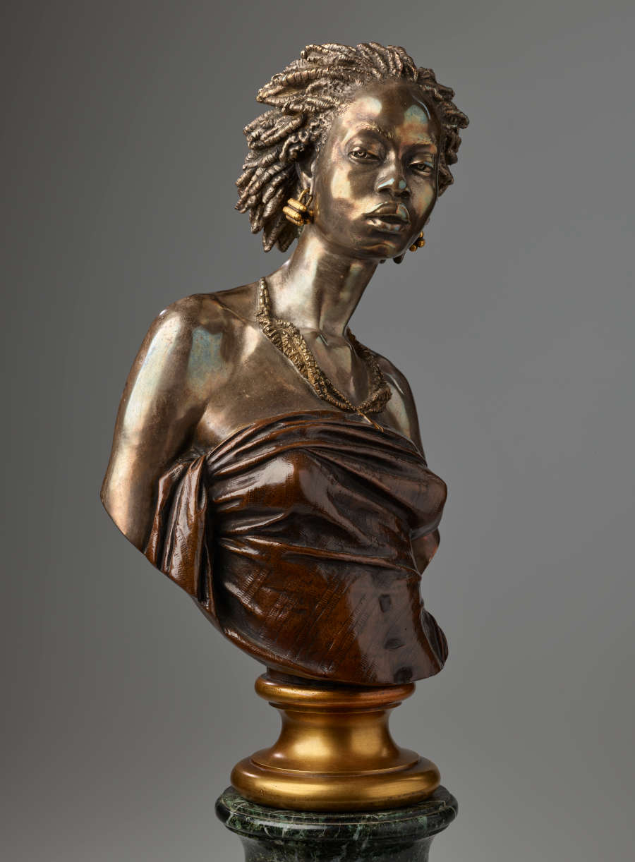 Bronze bust of a woman with raised chin, hair in twists, gold earrings, beaded necklaces, and shoulders exposed in a strapless wrapped dark top mounted on a gold base.