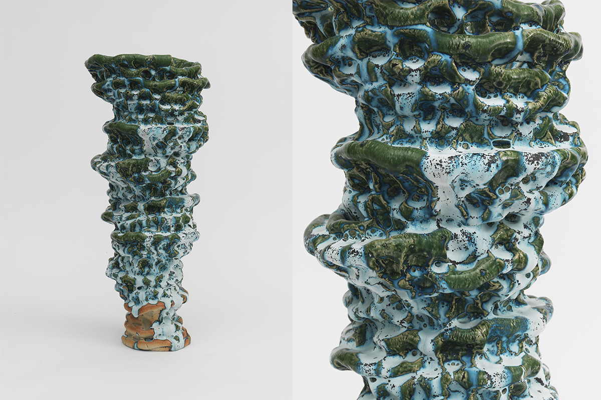A tall, textured ceramic sculpture with layered, irregular surface in glossy blue, green, and white glazes. The form resembles organic rock formations or coral. It is shown in full view and close-up.