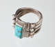 Three-quarters view of a silver metal ring with a rectangular turquoise stone setting embellished with nature-inspired and rope-like decorative elements. The band narrows towards its back.