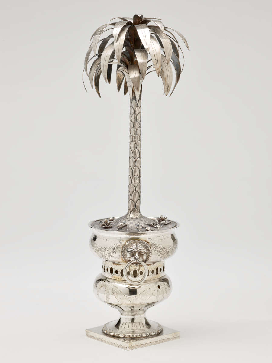 Silver sculpture in the shape of a palm tree, sitting inside an urn.