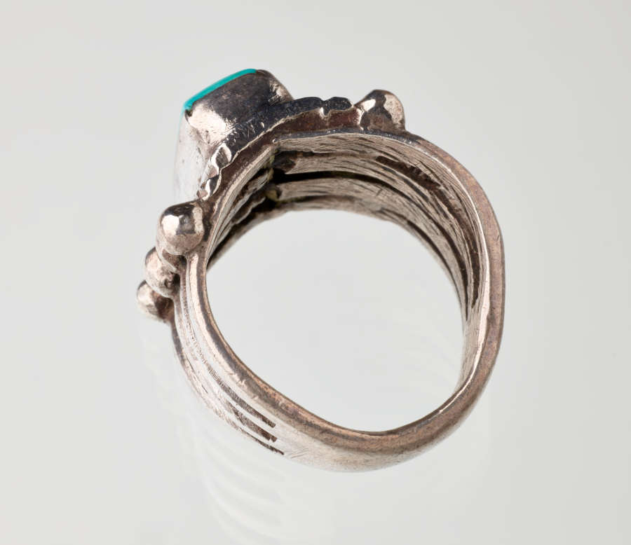 Top-view of a silver metal ring with a turquoise stone-setting. Visible are the inner grooves flowing across the band’s interior and towards the stone.