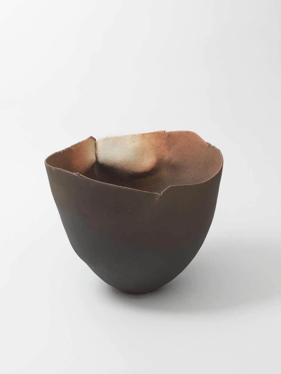 Hand-shaped dark ceramic bowl with a thin, uneven rim and softly rounded body, its smoky interior blending soft shades of cream, brown and black.