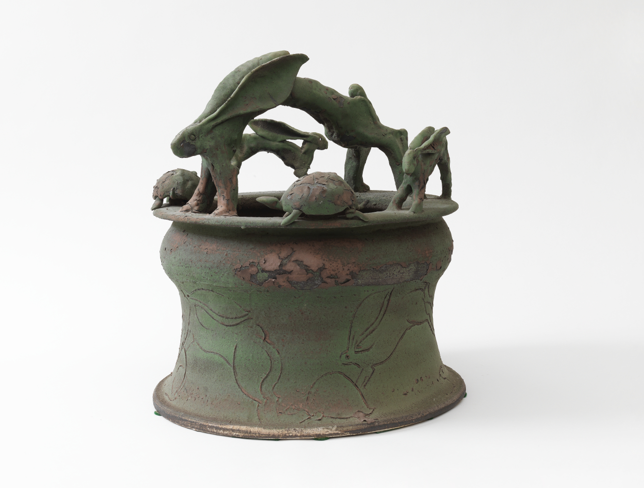An earthy green sculptural vessel with rabbits and turtles leaping and circling around the rim. The body is lightly etched with flowing line drawings of rabbits in motion.