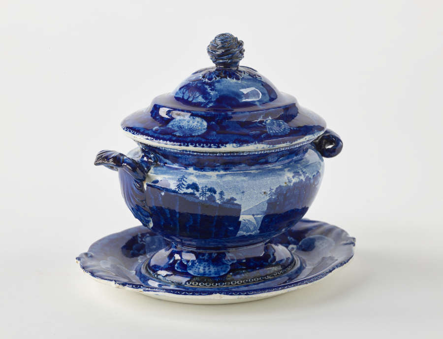  A dark blue decorative sauce boat. Two symmetrical sculptural handles that depict a bird’s head, foot, and lid with rounded finial