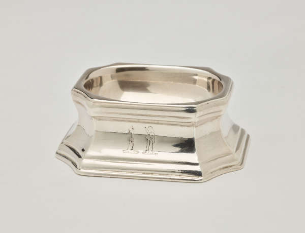 A silver salt container that is rounded on the inside and angular on the outside.