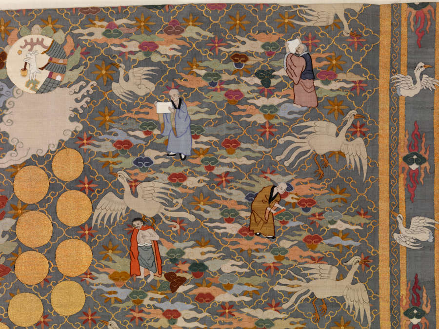 Top-right quarter of the robe’s back, featuring floral patterns overlaid by densely-packed illustrations of white birds, earthy-pastel clouds and robed humans. Concentrically-arranged golden circles are visible.