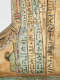 Close up of a coffin foot, decorated with vertical bands of hieroglyphs in black on a faded background.