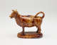  A brown sculptural creamer in the shape of a cow with horns. There is a small flat lid in the center of its back.