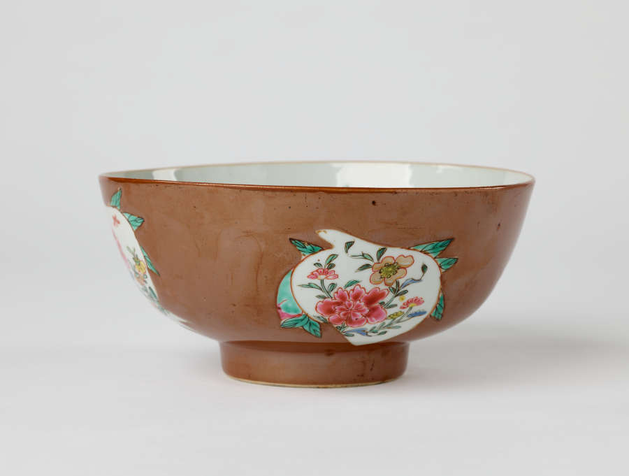 A white and brown bowl with green, yellow, and pink floral decorations with a short, small foot.