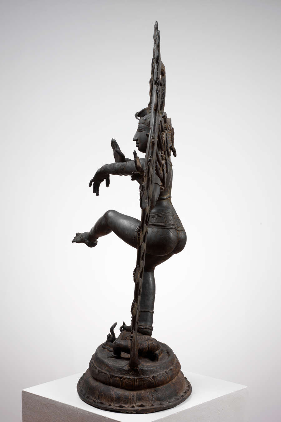 Side view of the bronze sculpture, showing the thin sculpted halo surrounding the figure and a truncated base. Two of the figure’s arms gesture outwards.