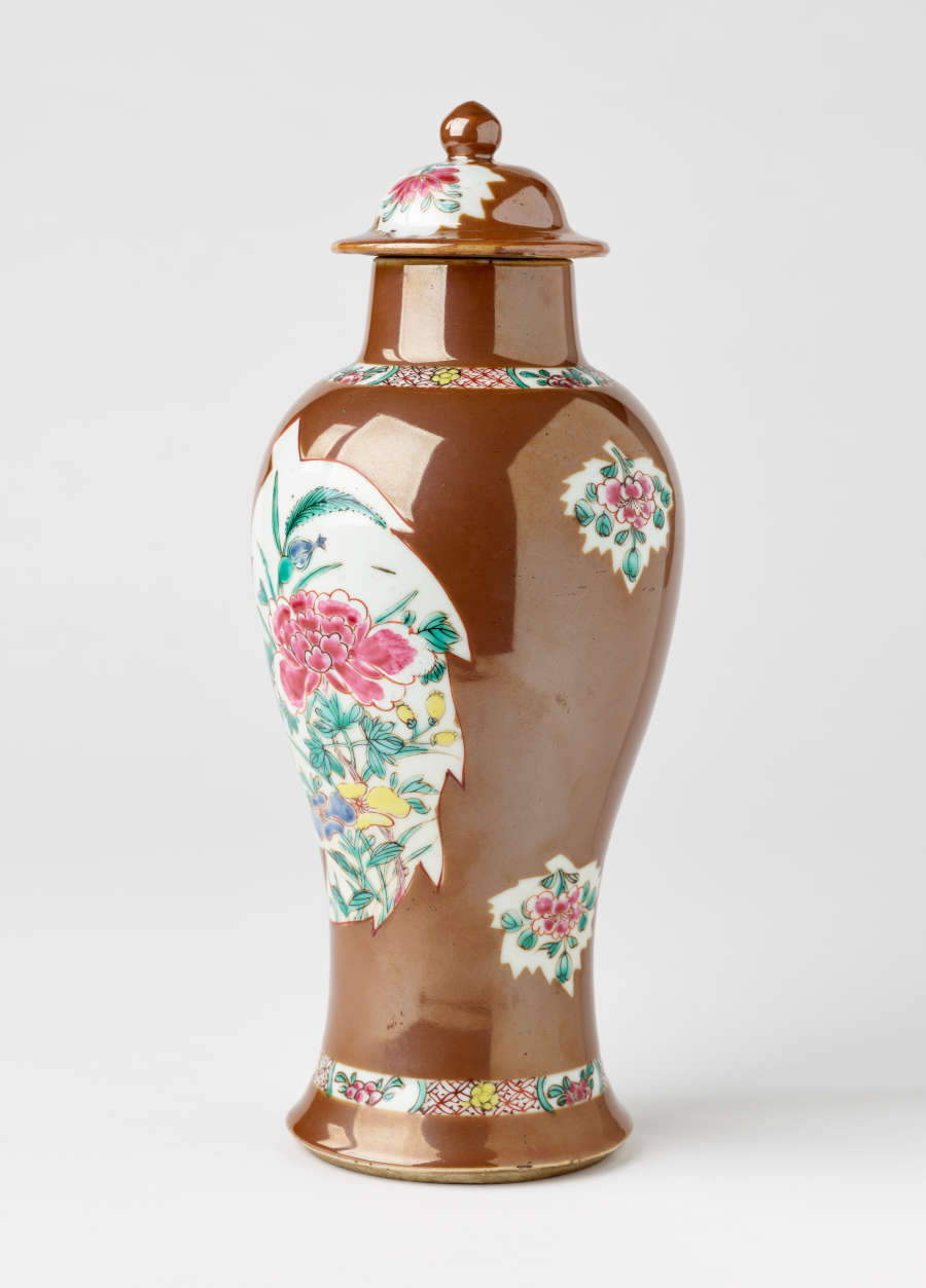 A brown and white covered vase with pink, green, blue, and yellow floral decorations.