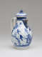 A white and blue chocolate pot with a spout, handle, and lid, the edges of the lid and spout are gilded. The decorations mainly depict floral, architectural, and landscape elements.