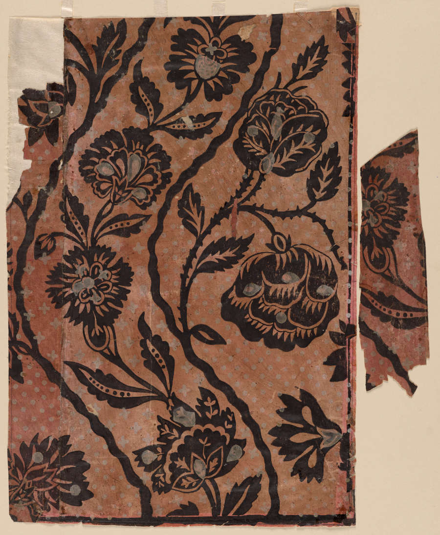 Fragment of vintage repetitive wallpaper depicting silhouetted chrysanthemums, curved vines and leaves. A smaller piece of wallpaper is torn off and placed to the right side of the larger portion.