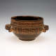 An earthenware bowl with a rounded form, dark interior, two side handles, lower brown half, and upper half with tan and brown geometric patterns. 