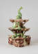 An elaborate, sculptural, three-tiered dish. Colored in brown, green, and cream with floral decorations as well as sculpted fish decorations.