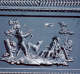 Gray rectangular panel with an elaborate decorative border and raised hunting scene of two figures, one standing holding an arrow aimed at a bird in flight and the other sitting.