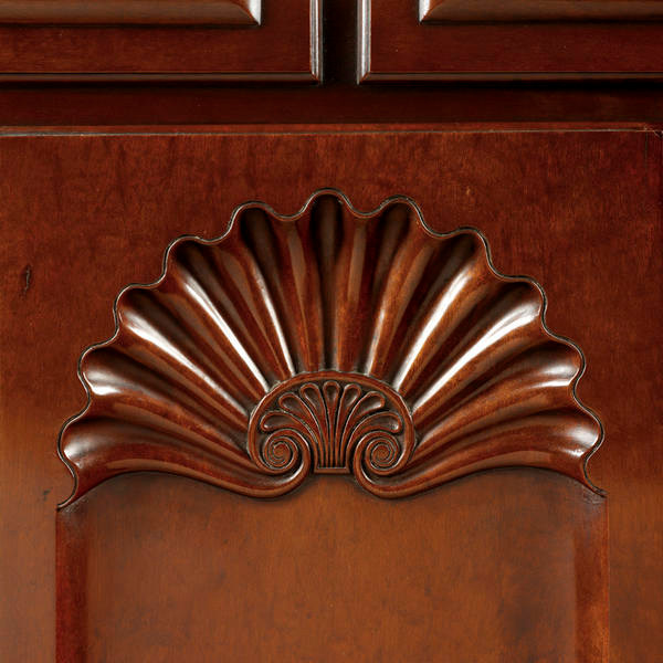 Design carved into dark brown wood featuring a motif of radiating grooves fanned out in a shell shape from a central detail depicting a petal pattern with two symmetrical spirals.