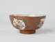 A white and brown bowl with green, yellow, and pink floral decorations with a short, small foot.