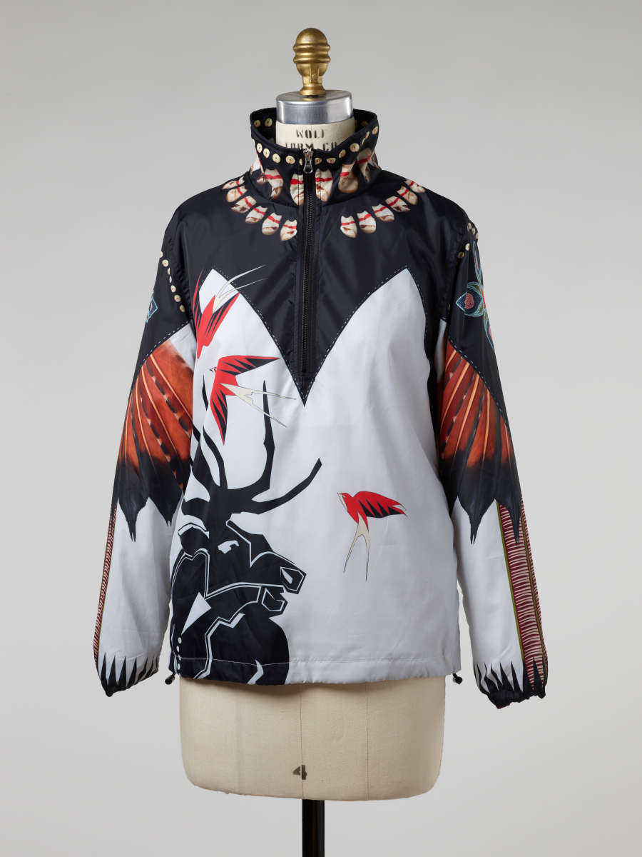 Windbreaker on a mannequin. The windbreaker features a black angular design at the top and red-orange feather and shell-motifs. The bottom is white with the silhouette of an antlered animal.