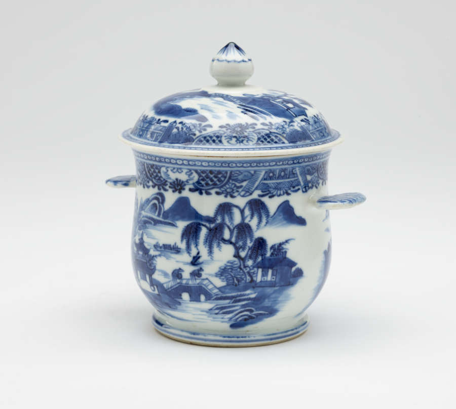 A white bowl with flat handles and lid. The blue decorations are architectural and floral.