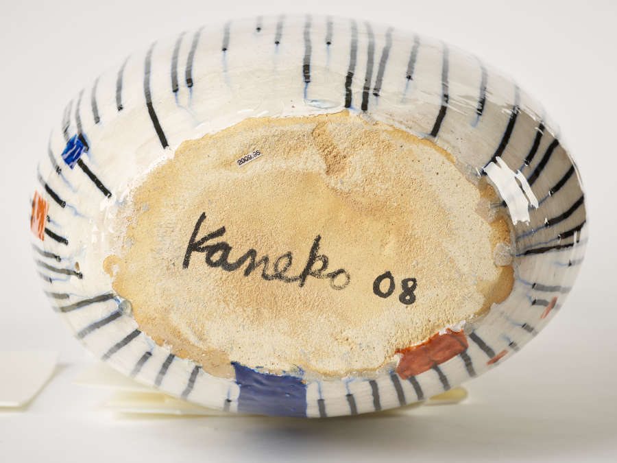 Base of a ceramic vase showing the artist’s signature and the piece’s year of creation: ‘Kaneko 08’. The unglazed base is surrounded by stripes and color blocks.